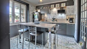 A modern kitchen with a central island, stainless steel appliances, and a large window providing natural light. - Villa Sérénité - PERROS GUIREC (PERROS GUIREC)