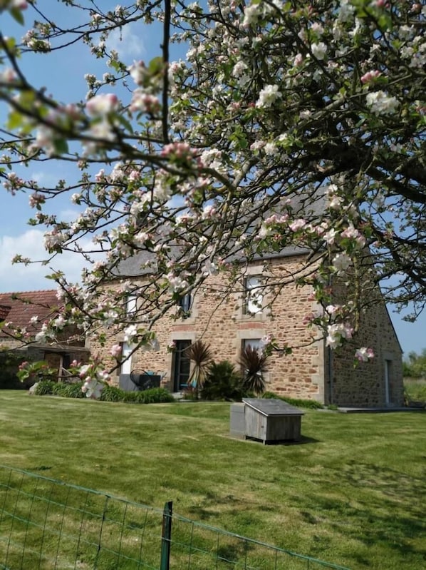 A stone building with a sloped roof, surrounded by a well-maintained lawn and a wire fence.