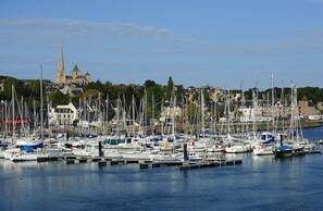 A marina with numerous boats docked, a prominent church with a tall spire in the background, and residential buildings along the shore.