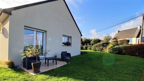 Una casa moderna con un césped cuidado, un patio con mobiliario exterior y un cielo despejado.