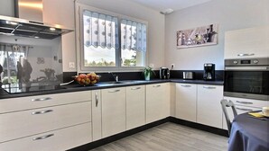A modern kitchen with white cabinets, a black countertop, a window with curtains, a coffee maker, and a microwave.