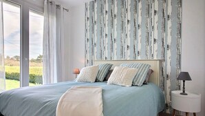 A bedroom with a large bed, a nightstand, and a view of a green landscape through a window.