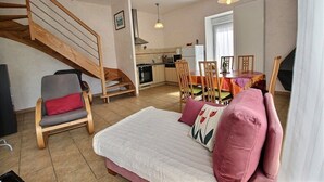 Een gezellige woonkamer met een bank, een eettafel met stoelen, een keuken en een houten trap.