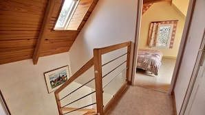 Een houten trap die leidt naar een slaapkamer met een bed en een raam met gordijnen.