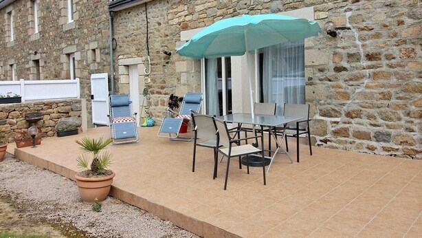 Een stenen gebouw met een patio, inclusief een tafel, stoelen, een blauwe parasol en potplanten.