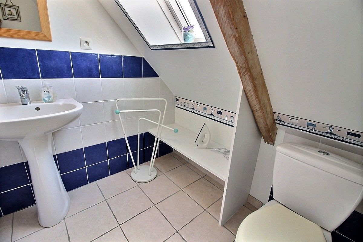 A bathroom with a white sink, blue-tiled walls, a white toilet, and a small window.