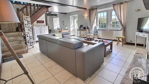 Un salón amplio con un sofá gris, una escalera de madera y un televisor sobre un mueble.