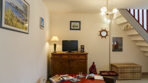 A cozy living room with a wooden cabinet, a television, and a dining table with magazines. - Kerborn - PLOUGUIEL - Gîte (PLOUGUIEL)