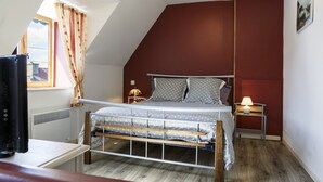 A bedroom with a sloped ceiling, a bed with grey polka dot bedding, a bedside lamp, and a radiator. - Kerborn - PLOUGUIEL - Gîte (PLOUGUIEL)