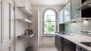 A modern kitchen with white cabinetry, a window, and a tiled backsplash. - Elegant, Airy 2 Bedroom Flat in Paddington (London)