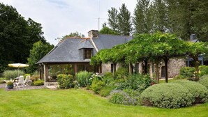 A stone house with a sloped roof, a covered patio, and a well-maintained garden with various plants and a lawn.