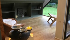 A modern interior with a wooden floor, a wicker chair, a large window, and a view of a green lawn.