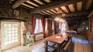 A rustic dining area with a wooden table and benches, stone walls, and a stone fireplace.