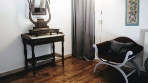 A room with a wooden floor, a small table with a mirror and a decorative object, a black chair, a patterned curtain, and a wall-mounted light fixture. - COSY 1/2 mile to sea (Livorno)