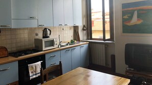 A kitchen with light blue cabinets, a microwave, a stove, and a window with a view of a building outside. - COSY 1/2 mile to sea (Livorno)