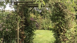 Un sentier de jardin qui traverse une tonnelle en bois recouverte d’un feuillage dense.