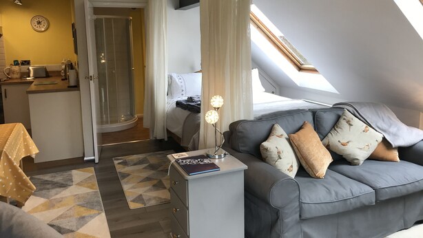 Une chambre moderne avec un lit, un canapé gris et un petit bureau avec une lampe.