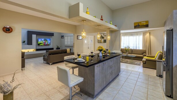 A modern kitchen with a central island, a dining area with a sofa, and a living room with a TV. - Sleeps 16 @ Palm Beach - 6BR Villa w/ Private Pool (Palm Beach)