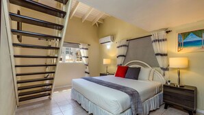 A bedroom with a bed, bedside tables, a window with curtains, a painting on the wall, and a staircase. - Sleeps 16 @ Palm Beach - 6BR Villa w/ Private Pool (Palm Beach)