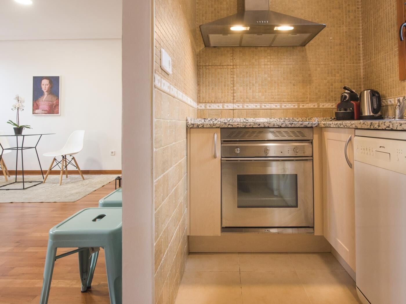 Een kleine keuken met een inbouwoven, een vaatwasser en een roestvrijstalen afzuigkap.