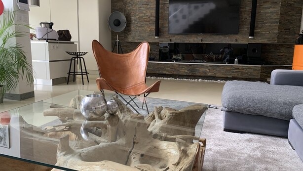 A modern living room with a glass coffee table featuring a natural wood design, a leather armchair, a grey sofa, and a flat-screen TV mounted on a stone wall. - Luxury loft with pool and garden (Avignon)