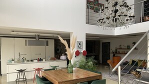 A modern kitchen with white cabinets, a stainless steel range hood, and a dining area with a wooden table and green chairs. - Luxury loft with pool and garden (Avignon)