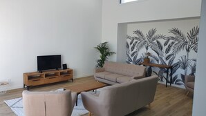 A modern living room with a sofa, coffee table, and TV stand. - Maison Neuve Proche mer Avec Piscine Chauffée (Fouesnant)