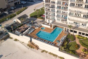 Ein Luftbild zeigt ein Hotel mit einem Dachpool, mehreren Balkonen und einer angelegten Gartenanlage.