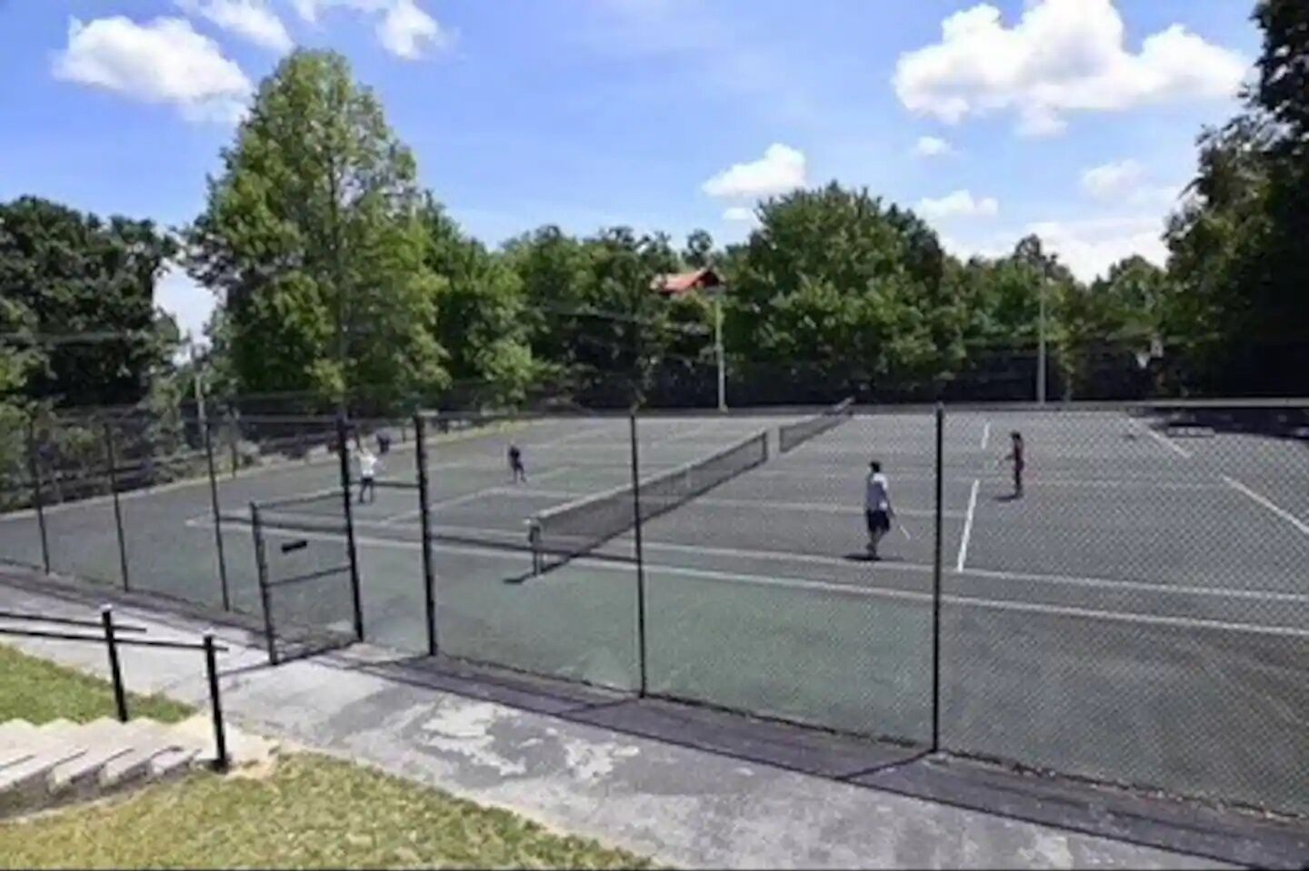 Un court de tennis avec un filet, entouré d’une clôture et d’arbres.
