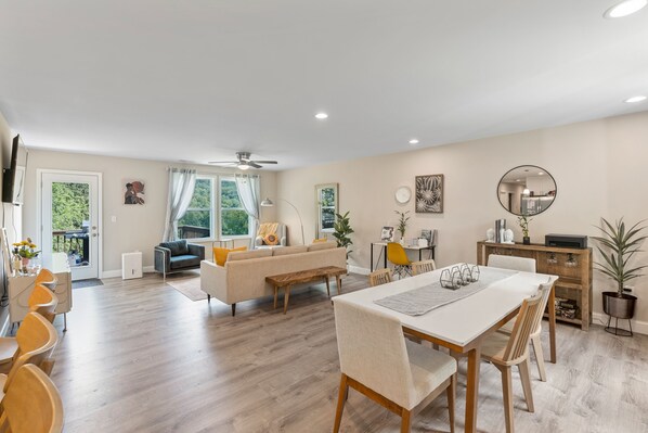 A spacious living area with a dining table, sofas, and a ceiling fan.