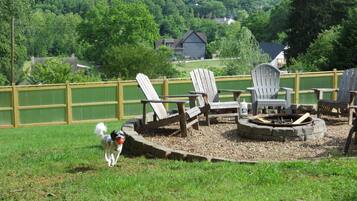 A backyard with a fire pit, Adirondack chairs, and a dog.