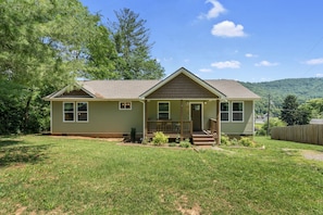 A single-story house with a front porch, a small front yard, and a view of a hilly landscape in the background.