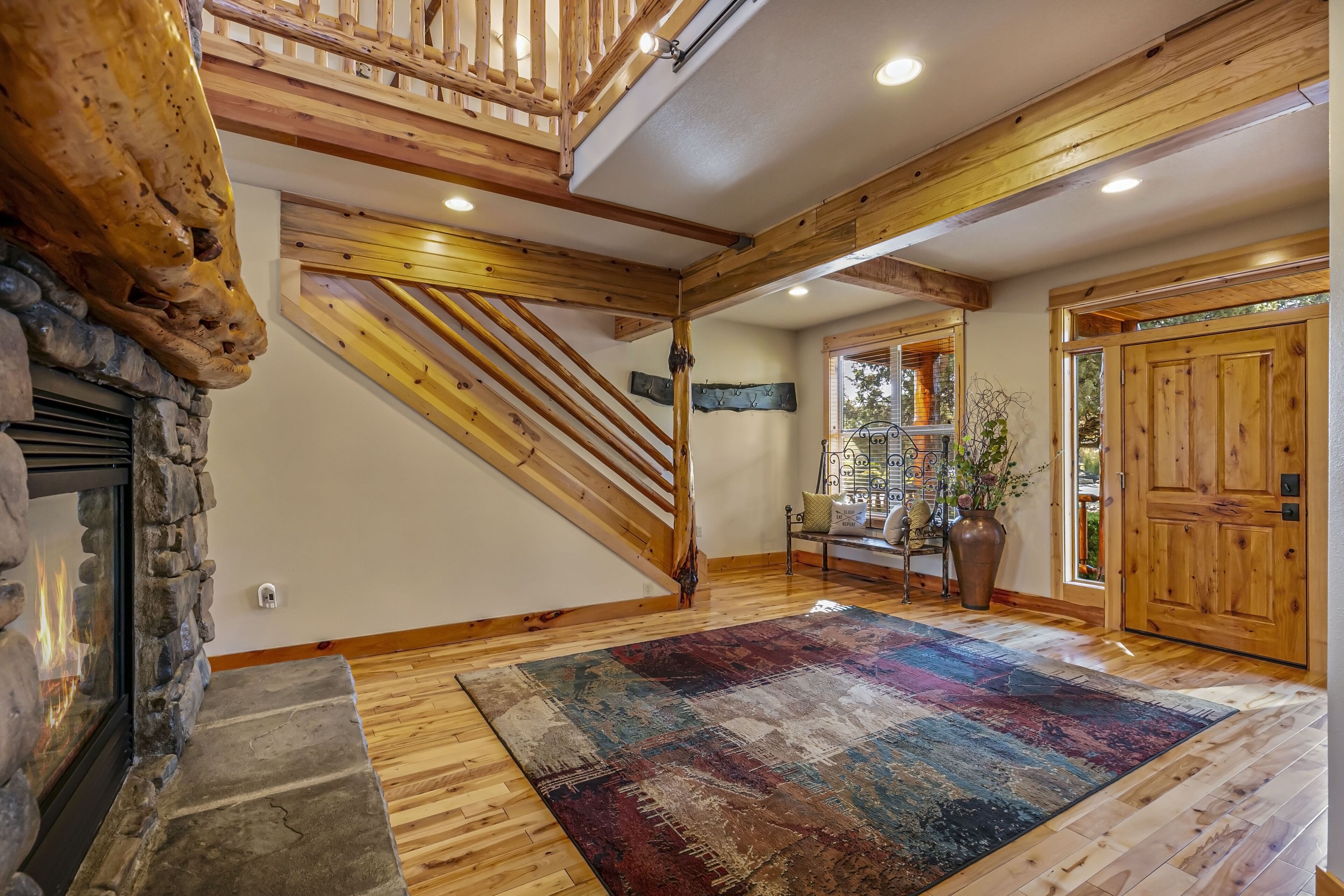 A spacious interior with a stone fireplace, wooden staircase, and a large rug on the floor.