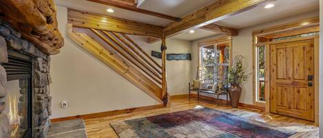 A spacious interior with a stone fireplace, wooden staircase, and a large rug on the floor.