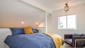 A bedroom with a large bed, a chair, a window, and a ceiling light fixture. - Dicky Bird Mount Washington Village (courtenay)