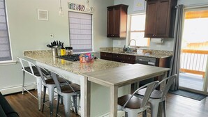 A kitchen with a central island, four bar stools, wooden cabinets, and a window with blinds. - The Aspen - in WPCO at 8488 ft elevation (Woodland Park)