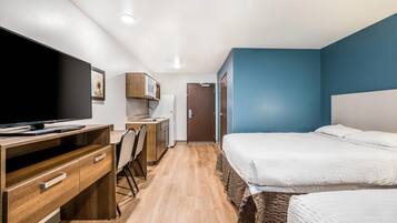 A compact hotel room with a bed, a desk with a computer, a microwave, and a small kitchenette.