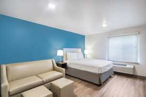 Habitación de hotel con cama, sofá, mesita de noche con lámparas y ventana con persianas.