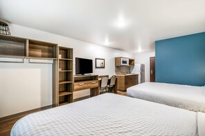 A hotel room with two beds, a desk with a chair, a television, a microwave, and a refrigerator. - WoodSpring Suites Elgin - Chicago (Elgin)
