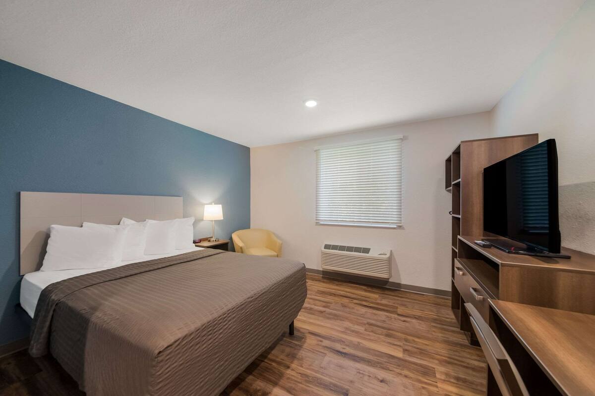 Une chambre d’hôtel équipée d’un lit, d’une télévision, d’une chaise, d’un bureau et d’une fenêtre avec des stores.