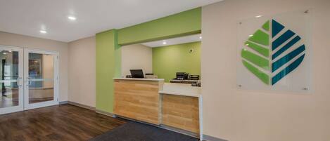 Un área de recepción con un mostrador de madera, una pared de acento verde y un logotipo grande con forma de hoja en la pared.