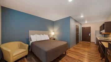 A hotel room with a bed, a chair, a desk, and a door.