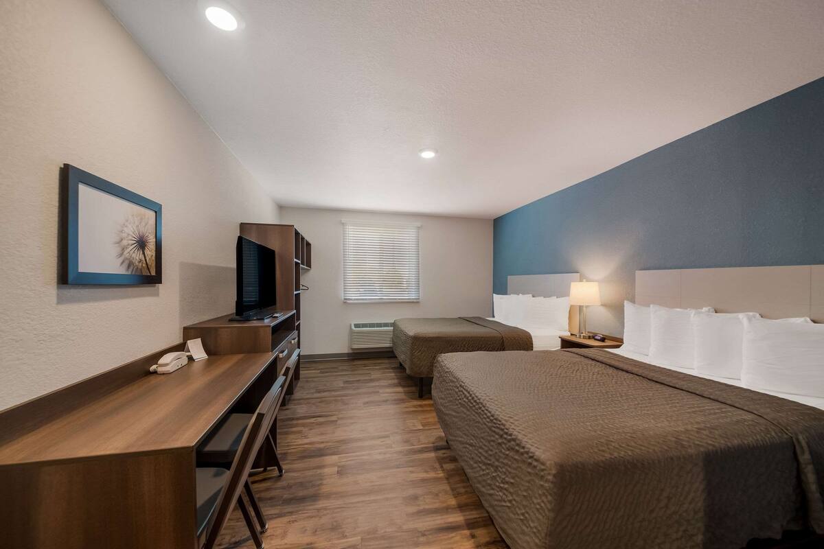 Une chambre d’hôtel équipée d’un bureau, de deux lits, d’une télévision et d’une fenêtre avec des stores.