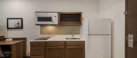 A compact kitchen with wooden cabinets, a white refrigerator, a microwave, and a sink.