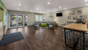 A modern living room with a sofa set, a coffee table, and a dining table with chairs. - WoodSpring Suites Wesley Chapel-Tampa (Wesley Chapel)