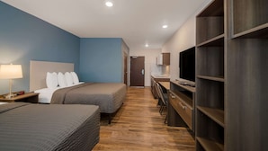 A hotel room with a bed, bedside table, lamp, and a TV on a stand. - WoodSpring Suites Wesley Chapel-Tampa (Wesley Chapel)