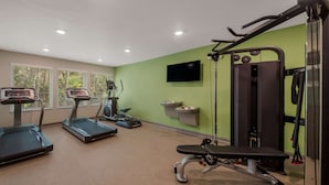 A gym with treadmills, a bench press, and a TV on the wall. - WoodSpring Suites Wesley Chapel-Tampa (Wesley Chapel)