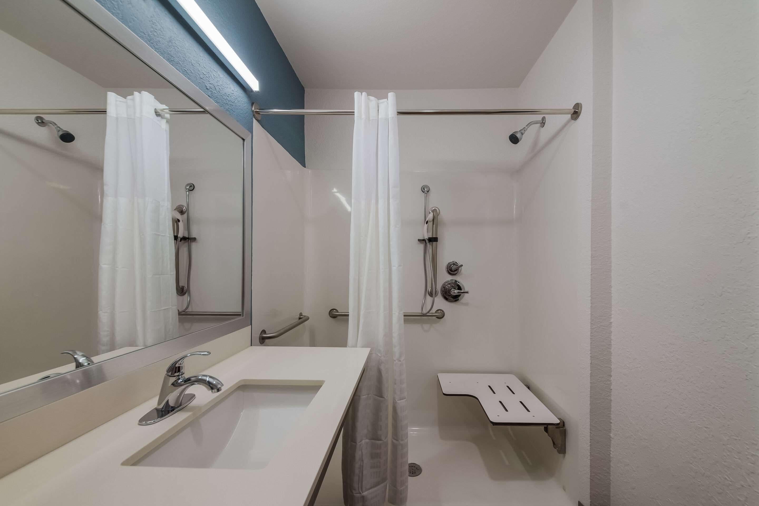 A modern bathroom with a large mirror, two sinks, a shower with a glass door, and a towel rack.