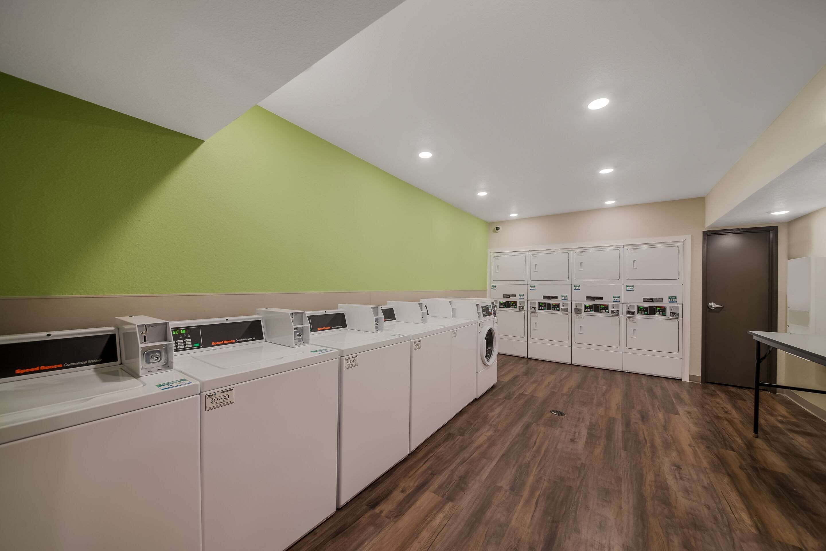 A laundry facility with multiple washing machines and dryers, a green wall, and a wooden floor.