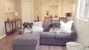Ein modernes Wohnzimmer mit einer Eckcouch, einem runden Couchtisch und einem Essbereich, im Hintergrund eine Küche.